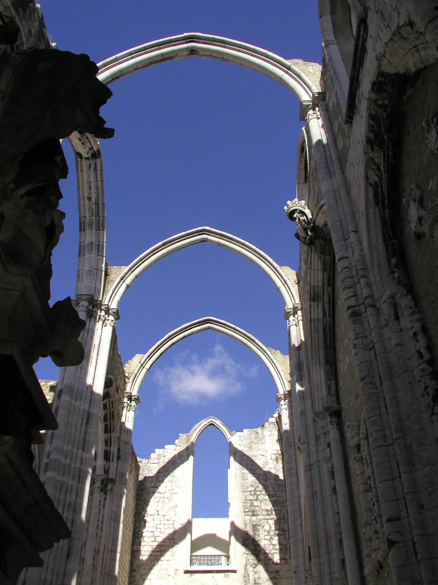 The roofless Gothic nave of the Carmo Convent in Lisbon, with a row of soaring pointed stone arches open against a deep blue sky