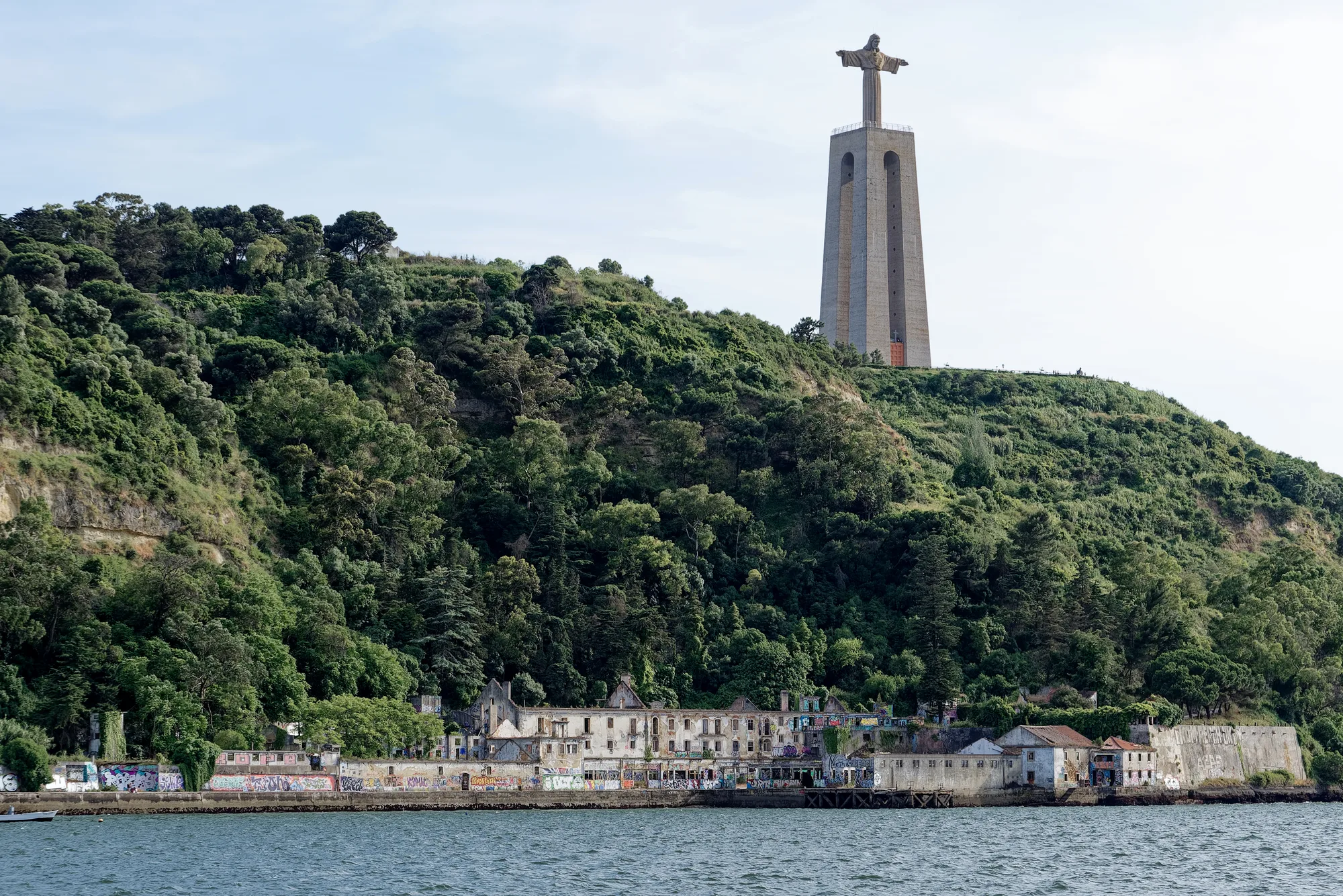 The Cristo Rei statue of Christ with open arms on its tall pedestal atop the green Almada cliff overlooking the Tagus, near Lisbon, Portugal