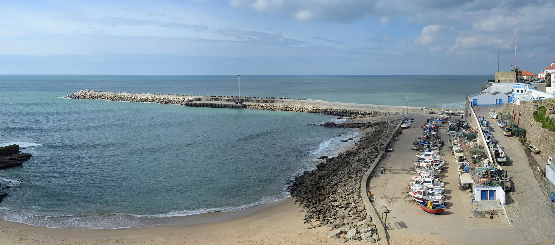 The Atlantic coastline at Ericeira with its breakwater, harbour beach and whitewashed houses of the surf town stacked on the cliff, Portugal