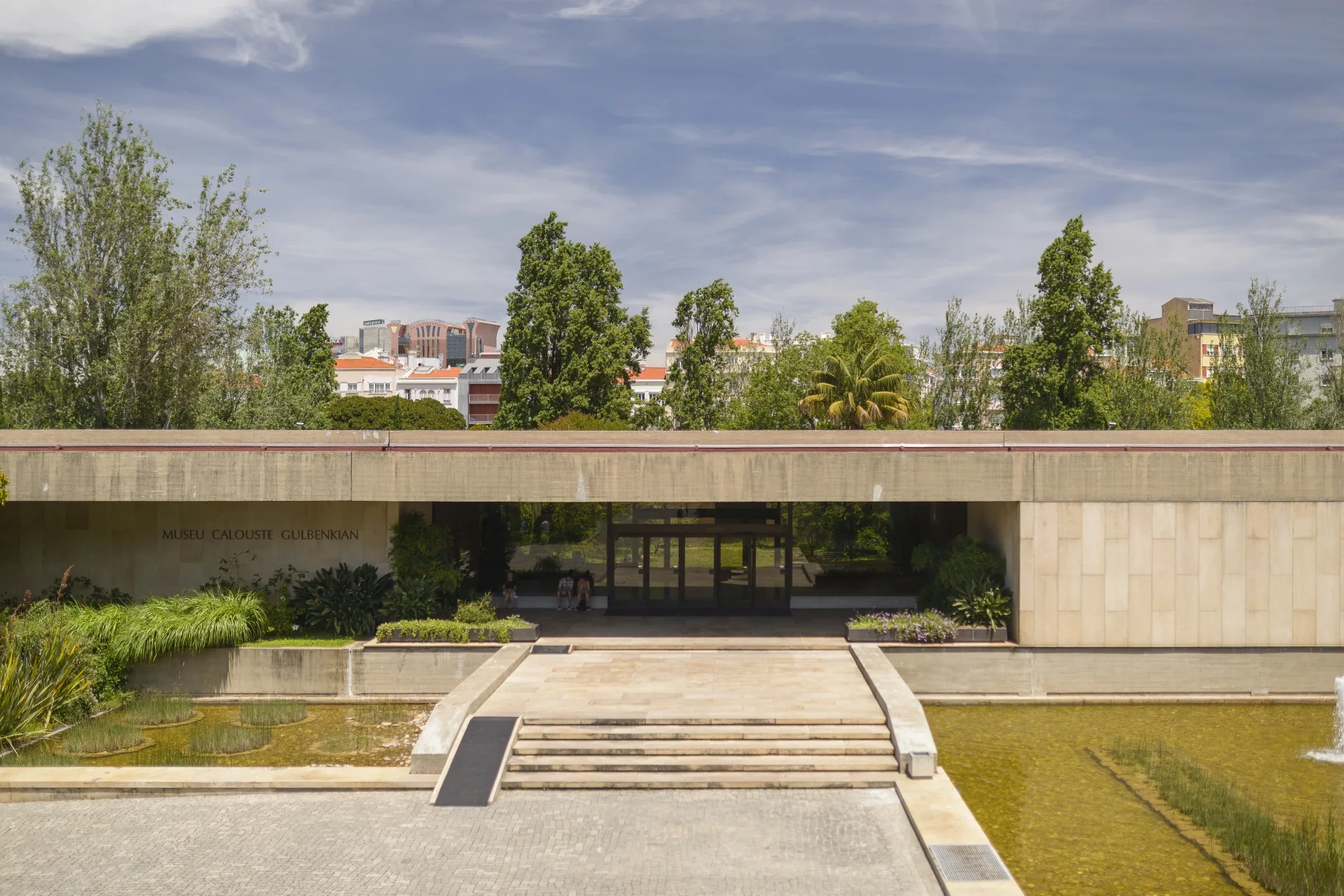 The modernist Calouste Gulbenkian Museum building in Lisbon with its low stone facade, name sign, reflecting pools and landscaped gardens