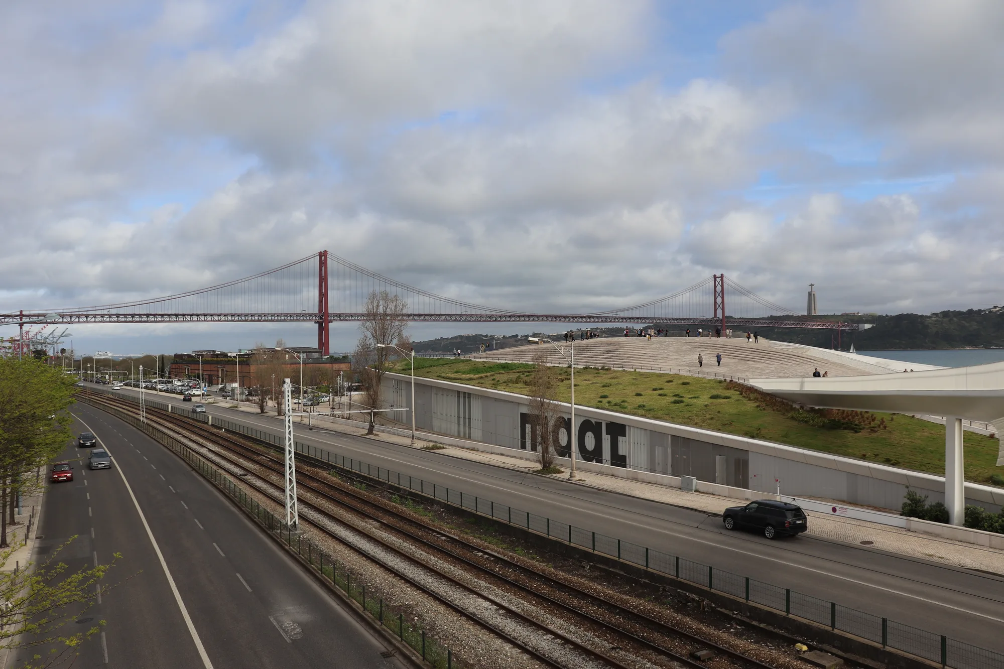 The sleek low white curved MAAT museum with its walkable wavy roof on the Tagus riverfront in Belém, Lisbon, with the 25 de Abril Bridge and Cristo Rei behind