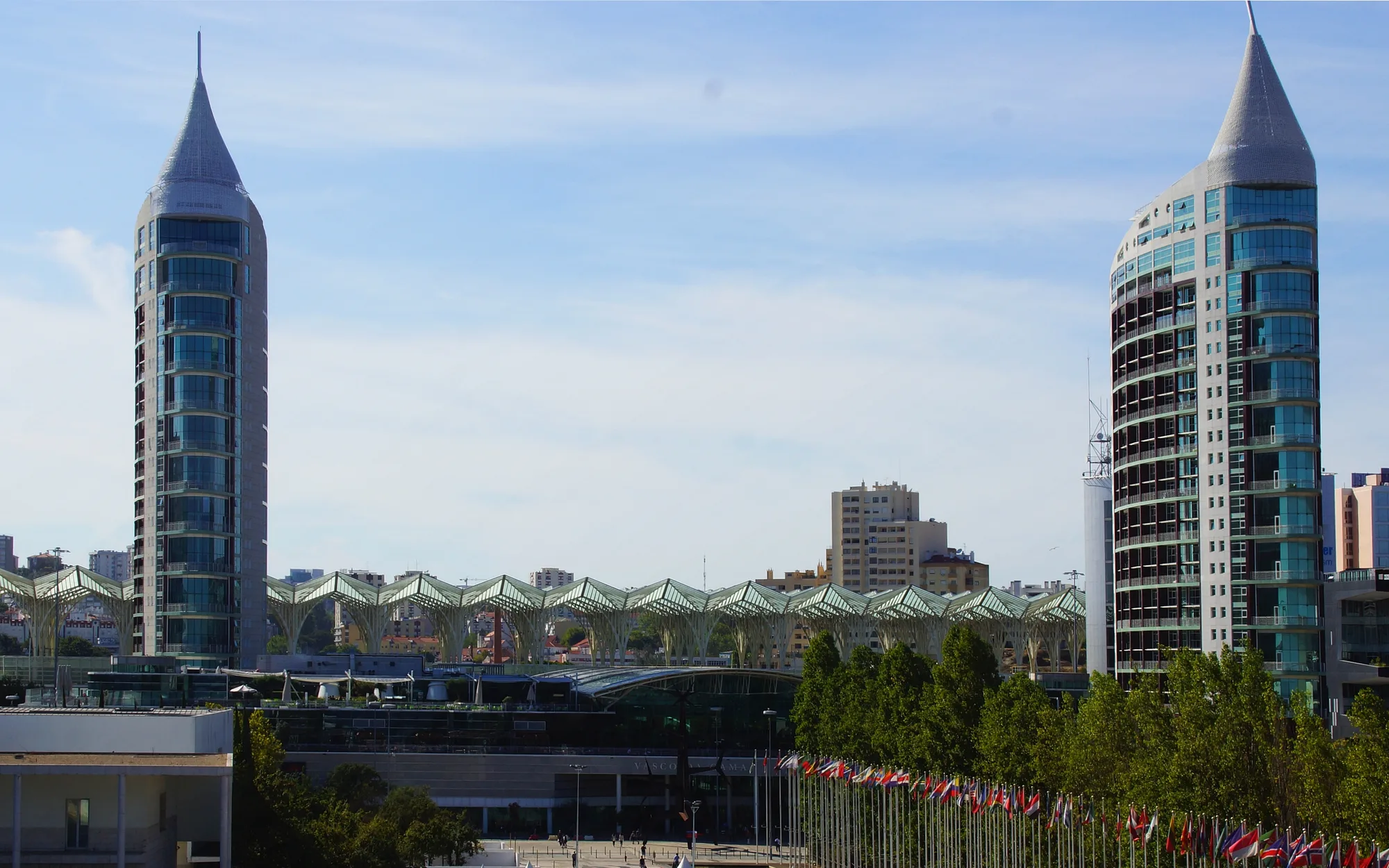 Modern Parque das Nações district skyline in Lisbon: the twin São Rafael and São Gabriel towers framing the wavy crystalline roof of Gare do Oriente, with the flag plaza in front