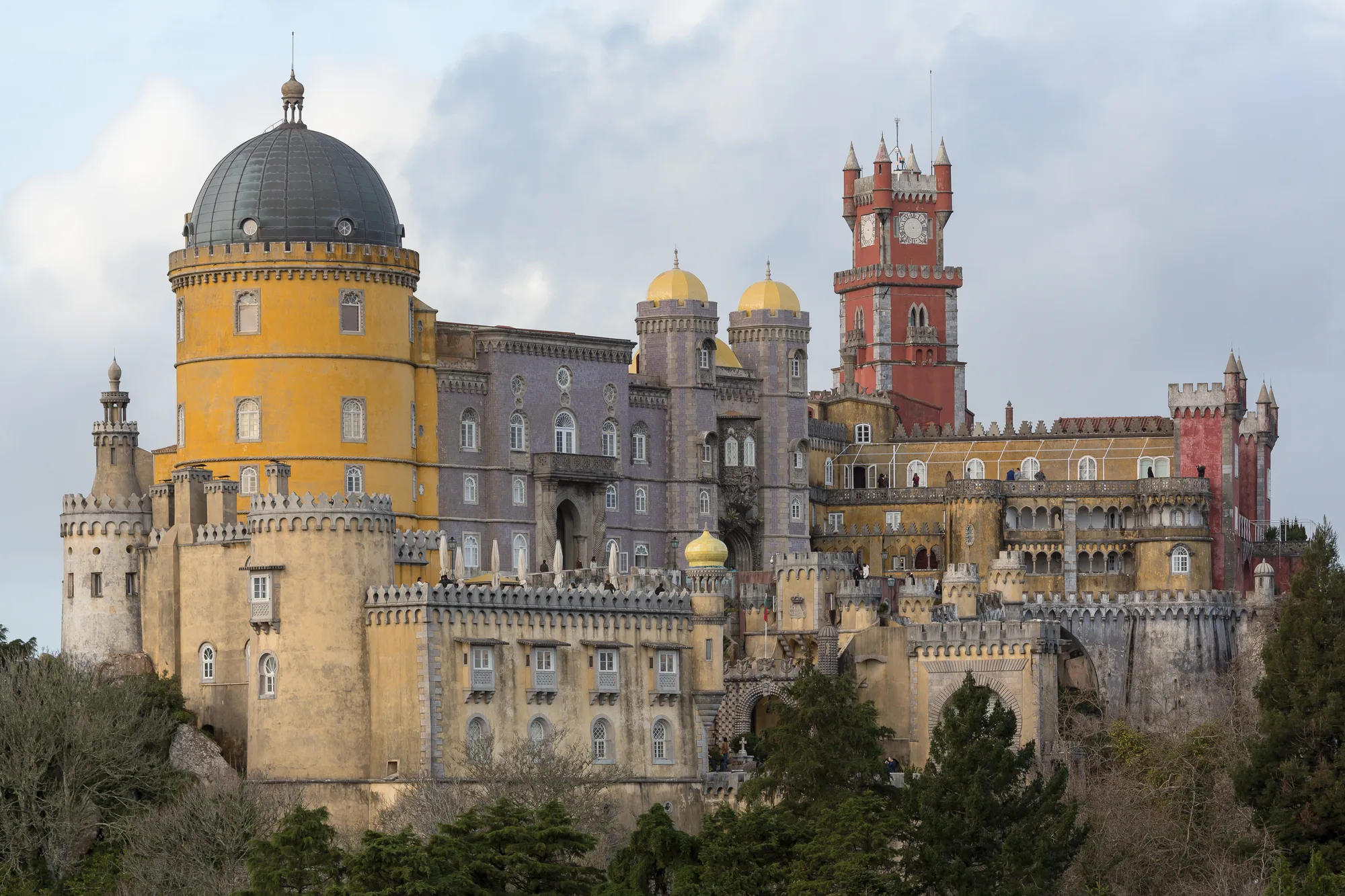 The colorful Pena Palace in Sintra, Portugal, showing its red clock tower, yellow domes and grey crenellated towers on the hilltop