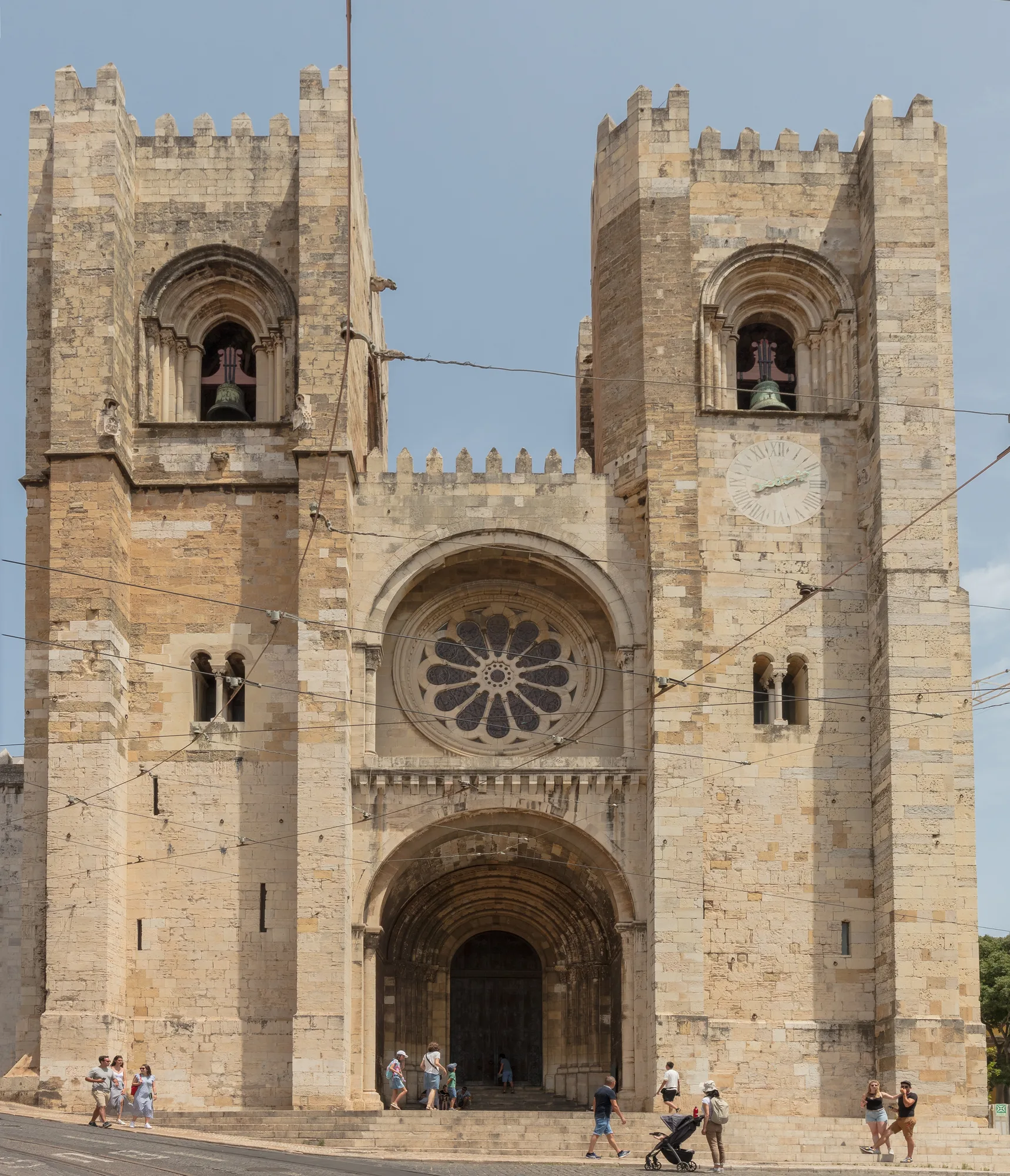 The fortress-like Romanesque west facade of Sé de Lisboa (Lisbon Cathedral) with its two crenellated bell towers, central rose window and arched portal, under a clear sky